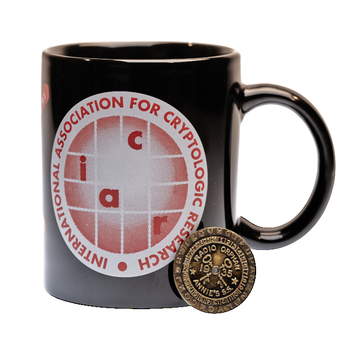 A 1935 Radio Orphan Annie's Secret Society decoder badge resting on a souvenir mug from the CRYPTO '93 conference.