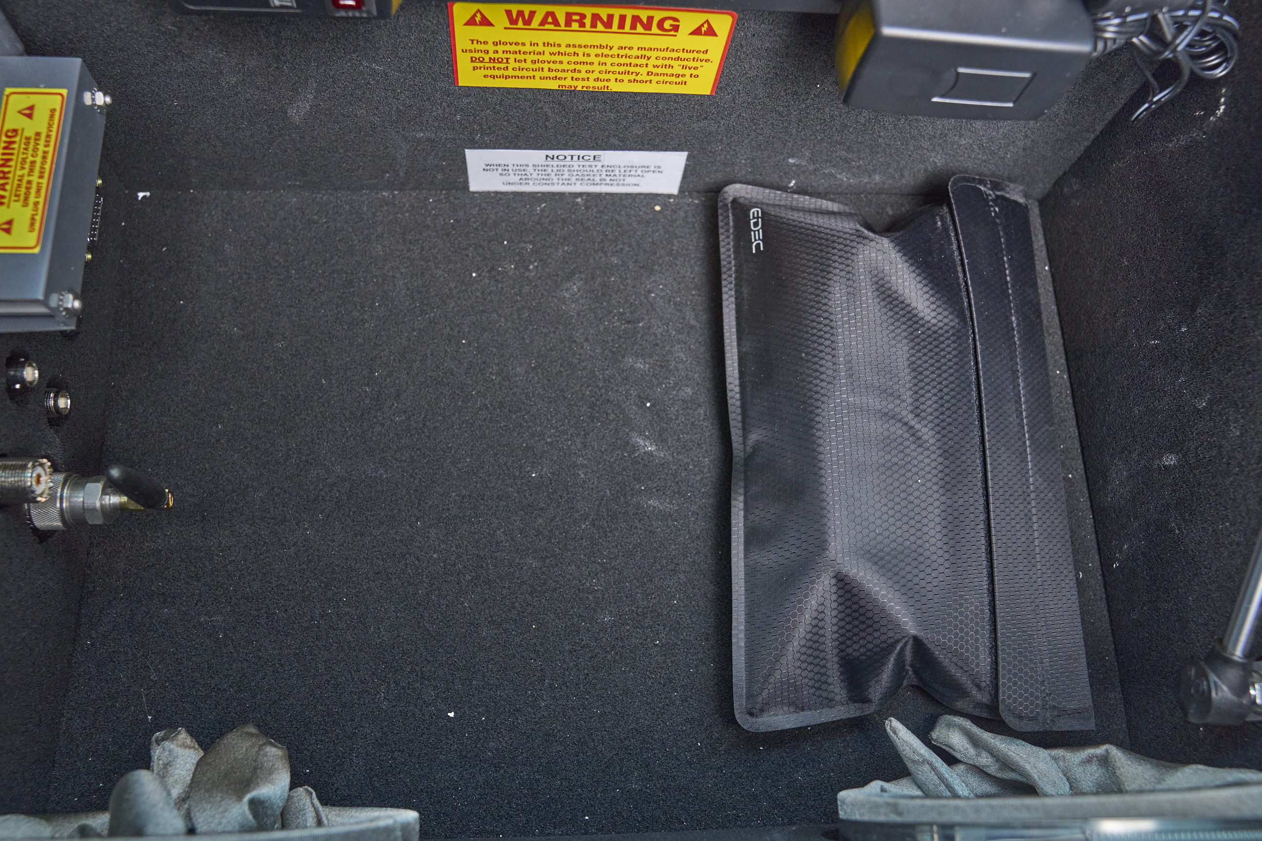Photo: The inside of the RF test chamber, with a no-nonsense windowless black pouch containing the signal generator. A slight hexagonal weave pattern is visible, and an EDEC logo in a corner.