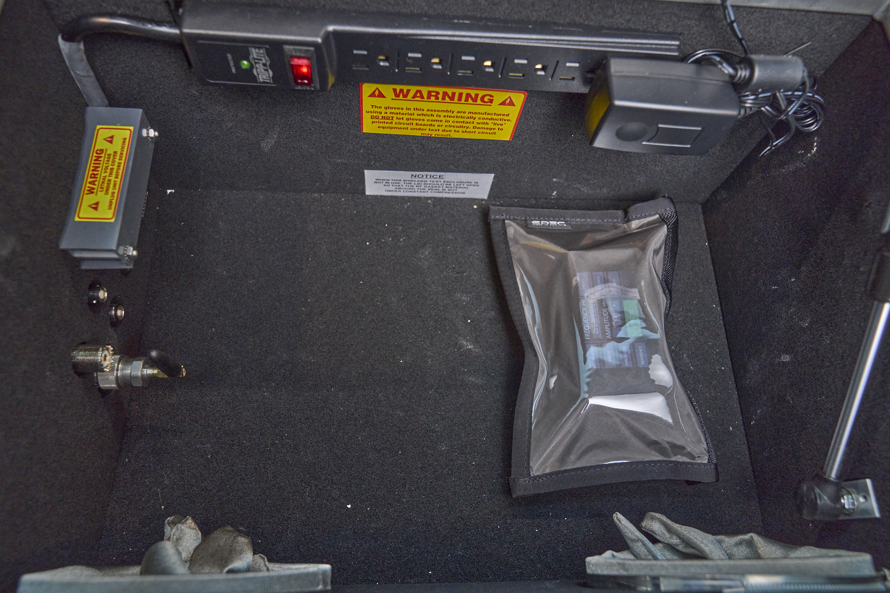 Photo: The inside of the same RF test chamber, but where the previous photo showed a signal generator, this one now shows a bulging outline of a signal generator visible through a clear plastic window of a pouch.